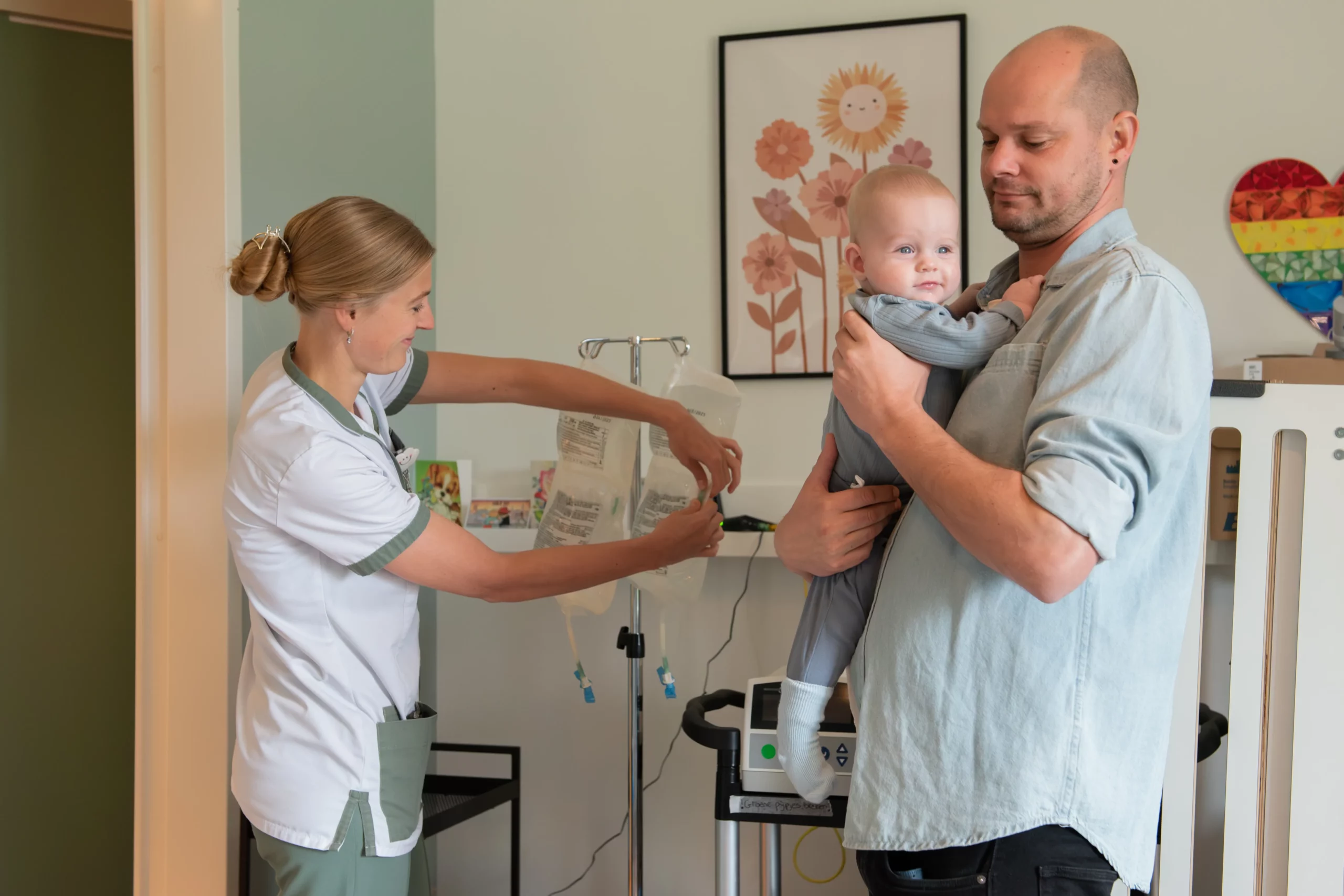 Vader tilt kind op en verpleegkindige bezig met infuus